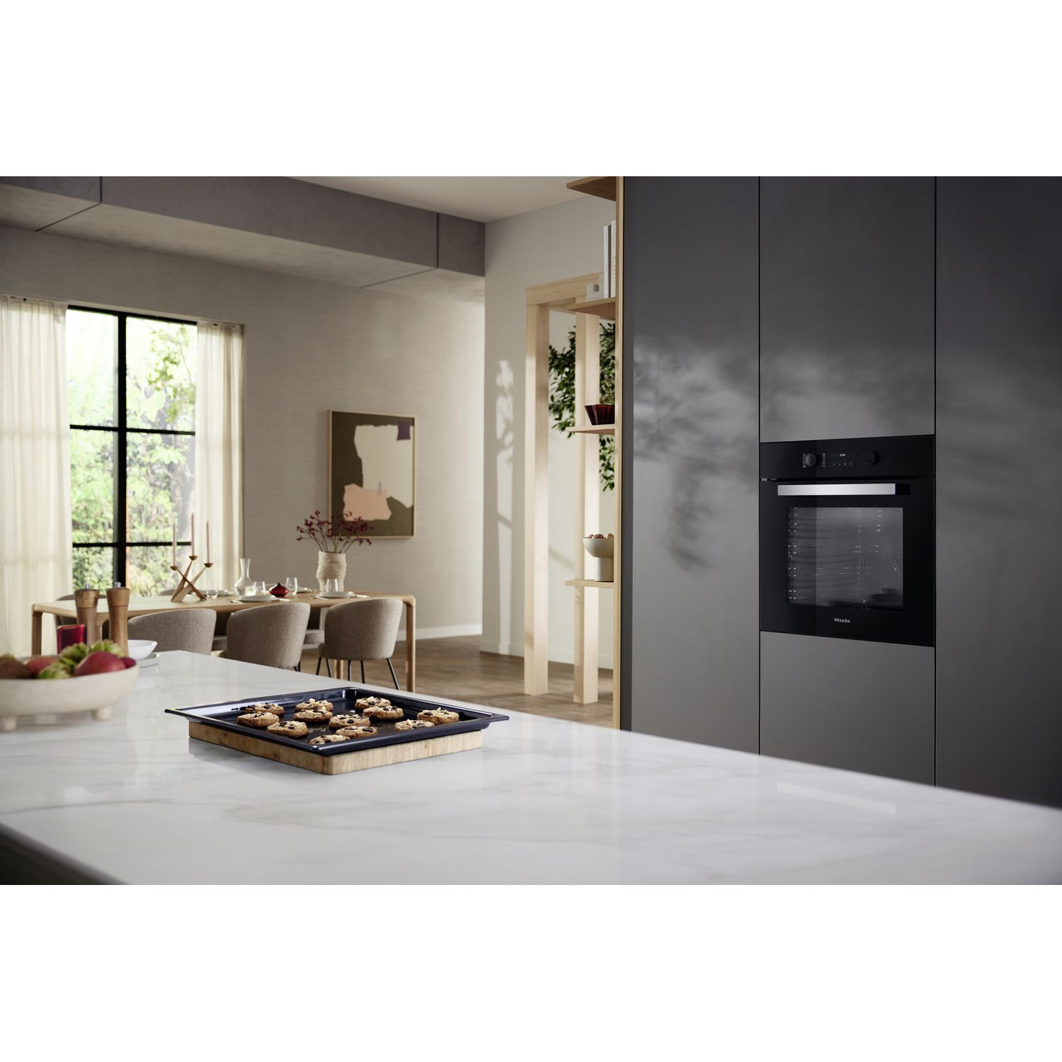 Moderne keuken met oven. Dienblad met bakwaren op aanrecht. Eettafel op de achtergrond.