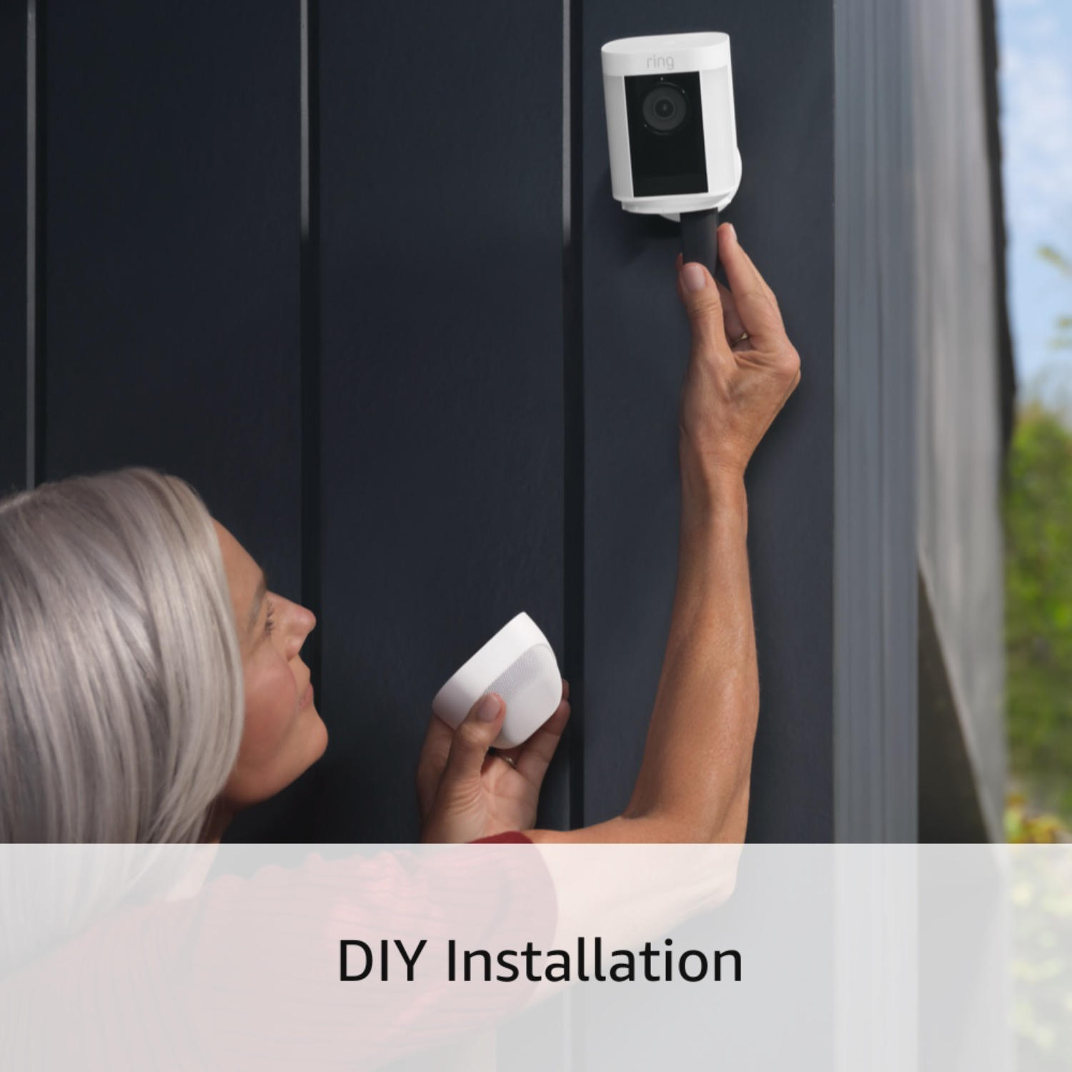 A woman installs a white Ring security camera on a dark wall.