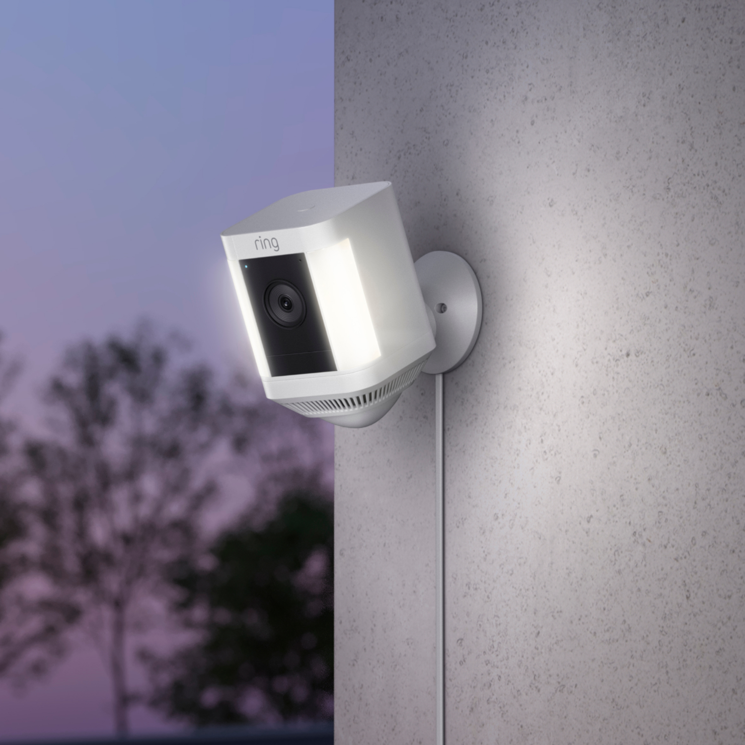 White Ring security camera mounted on a gray wall, angled, with a lit-up white light.