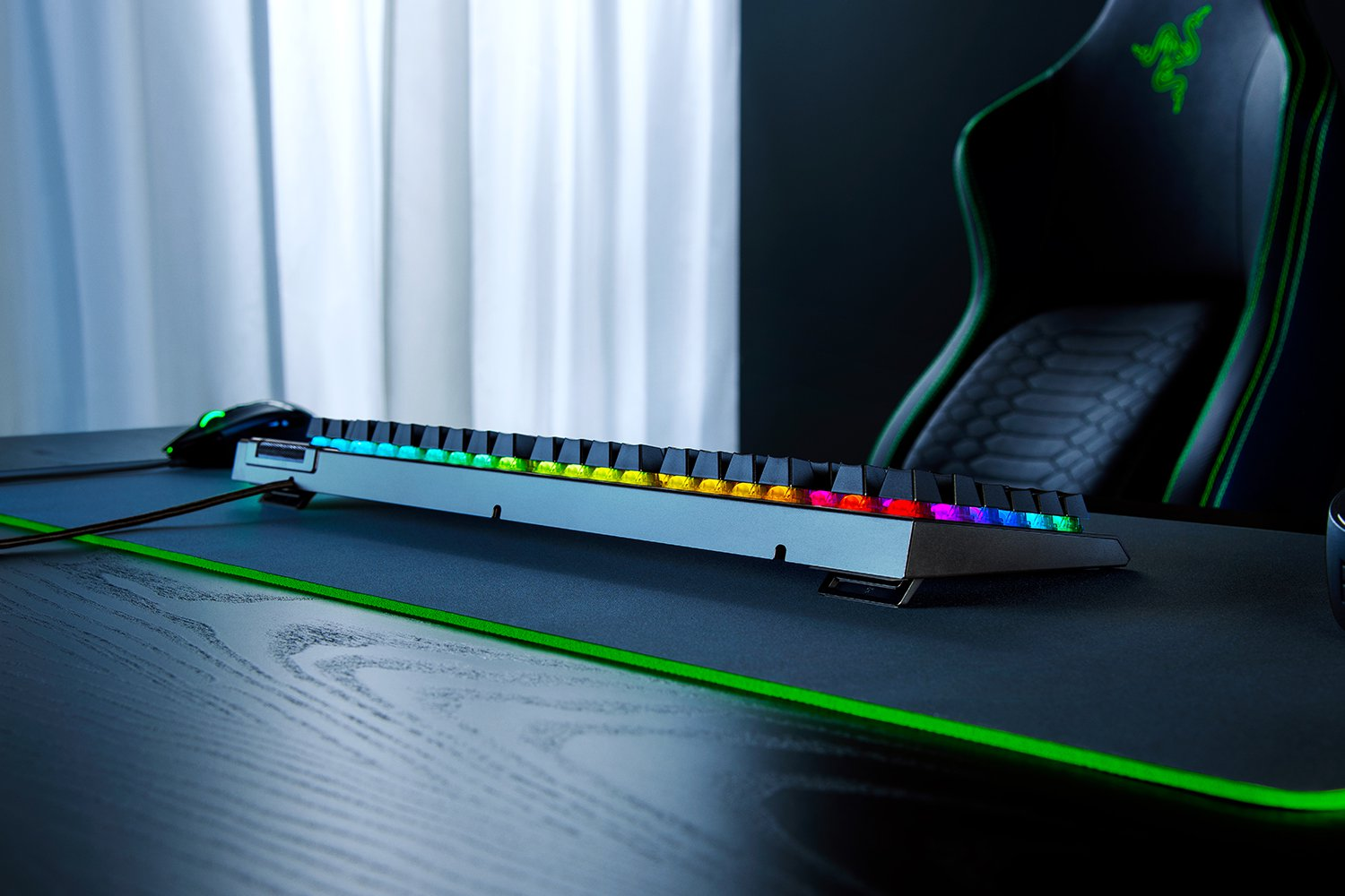 Teclado gaming con luces coloridas. Logo Razer arriba. Escritorio negro y silla Razer.