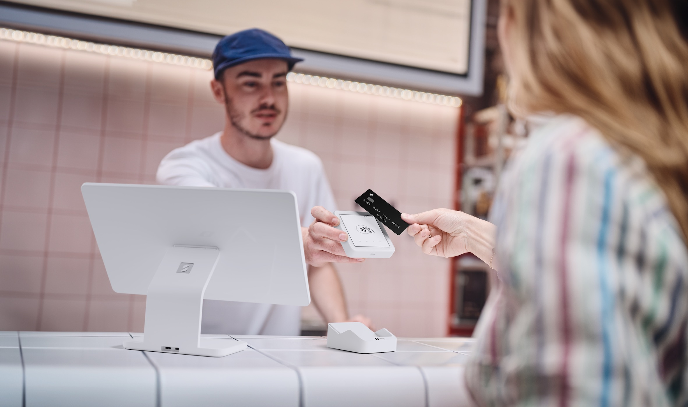 Una clienta pagando con tarjeta en una terminal POS. Un hombre con gorra azul la atiende.