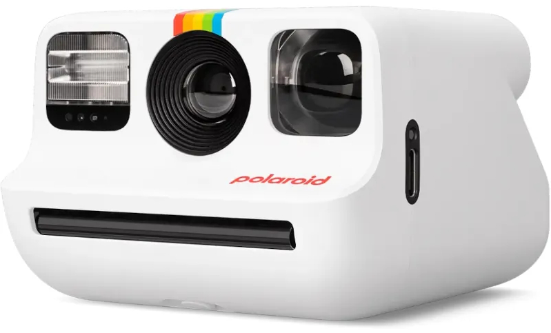 Biały aparat Polaroid. Posiada lampę błyskową, obiektyw i gniazdo na zdjęcia. Posiada tęczowy pasek.