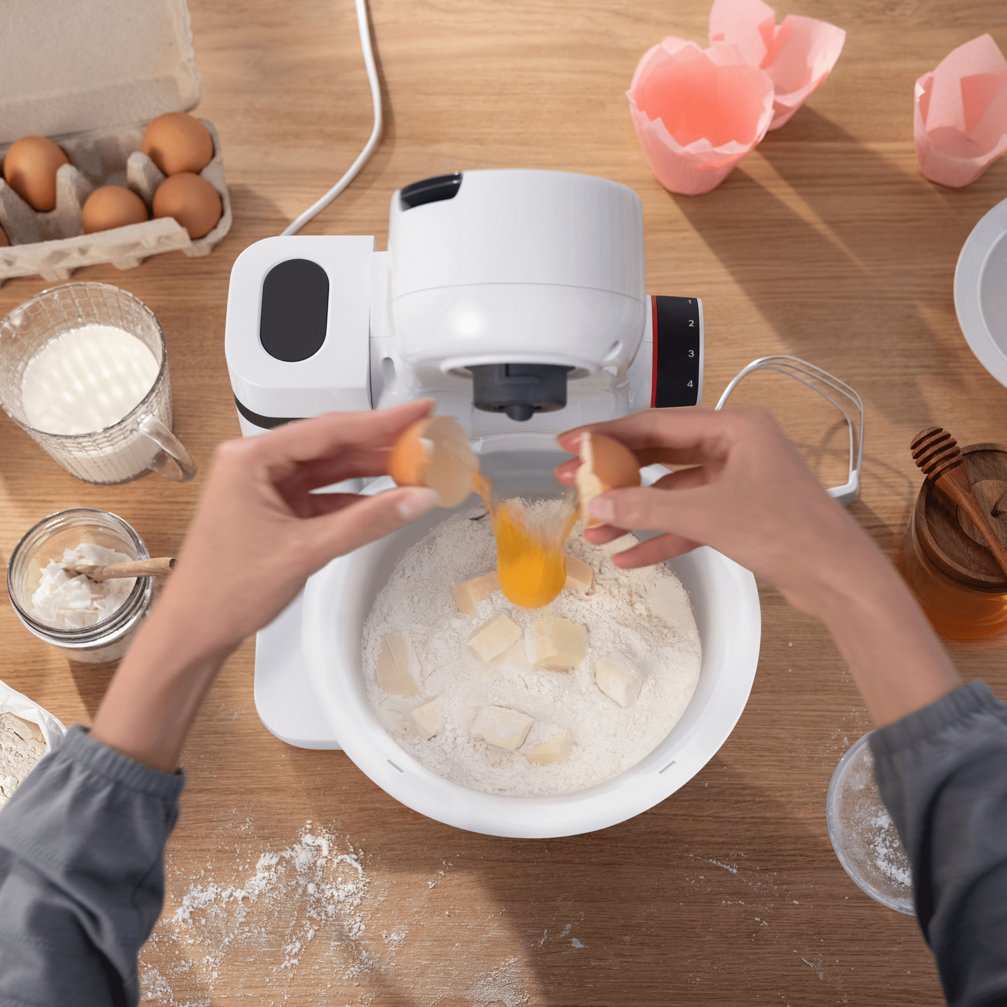 Hände schlagen Eier in eine Schüssel mit Mehl, Butter und einem Küchenmixer auf einem Holztisch.