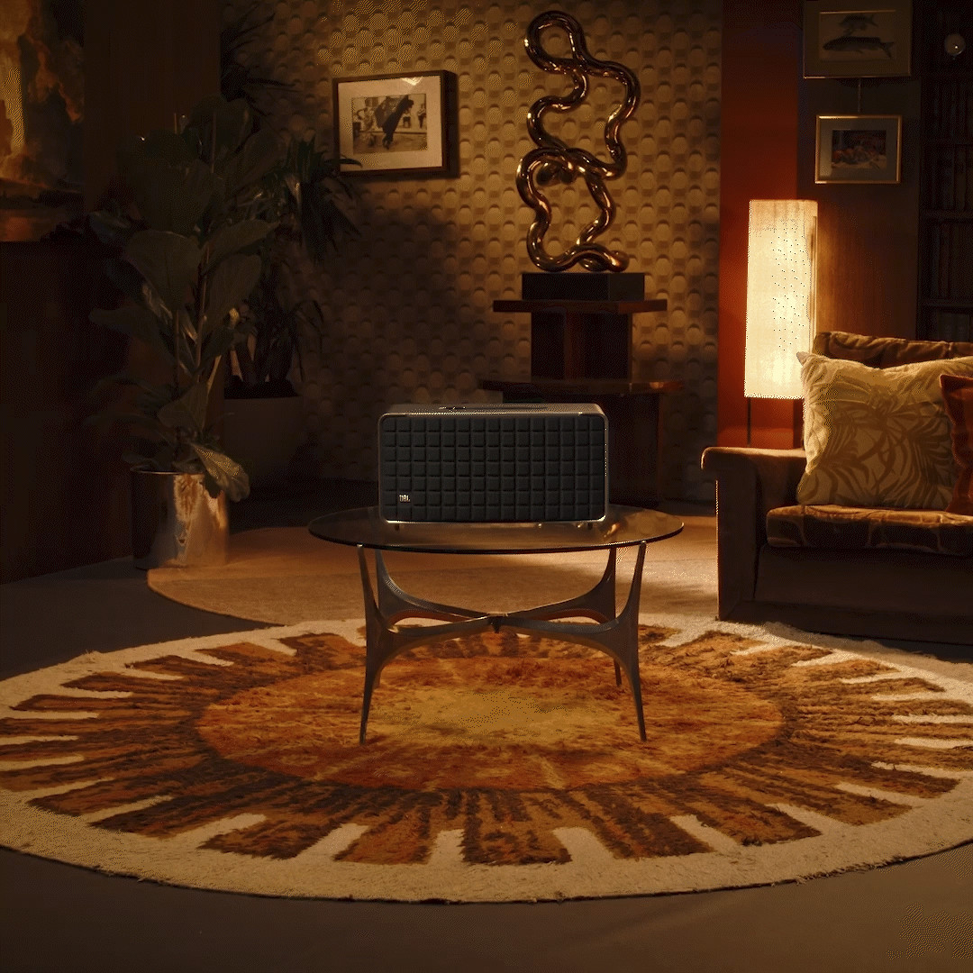 Une scène de salon avec un haut-parleur sur une table, entouré de décorations et d'un tapis avec un motif de soleil.