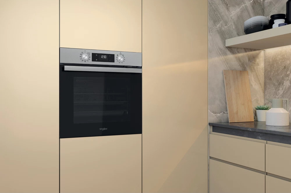 A modern kitchen with a built-in Whirlpool oven, showing the oven controls and display, beige cabinets.