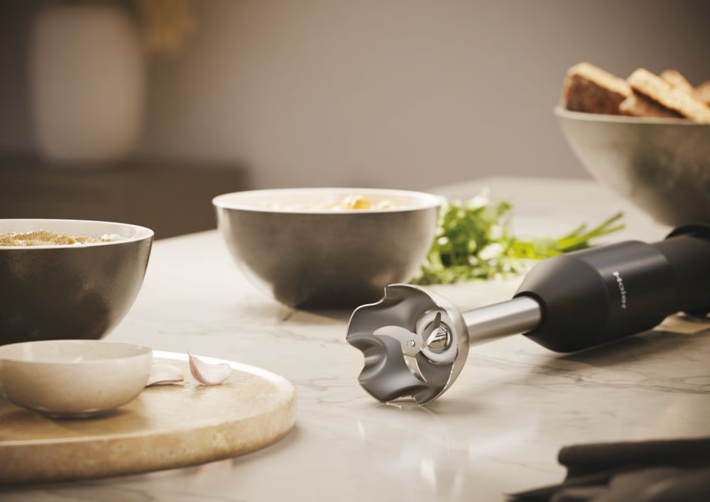 Mermer bir yüzeyde çorba kaseleri ve sarımsak bulunan bir el blenderi. Blenderin bıçağı görünür.