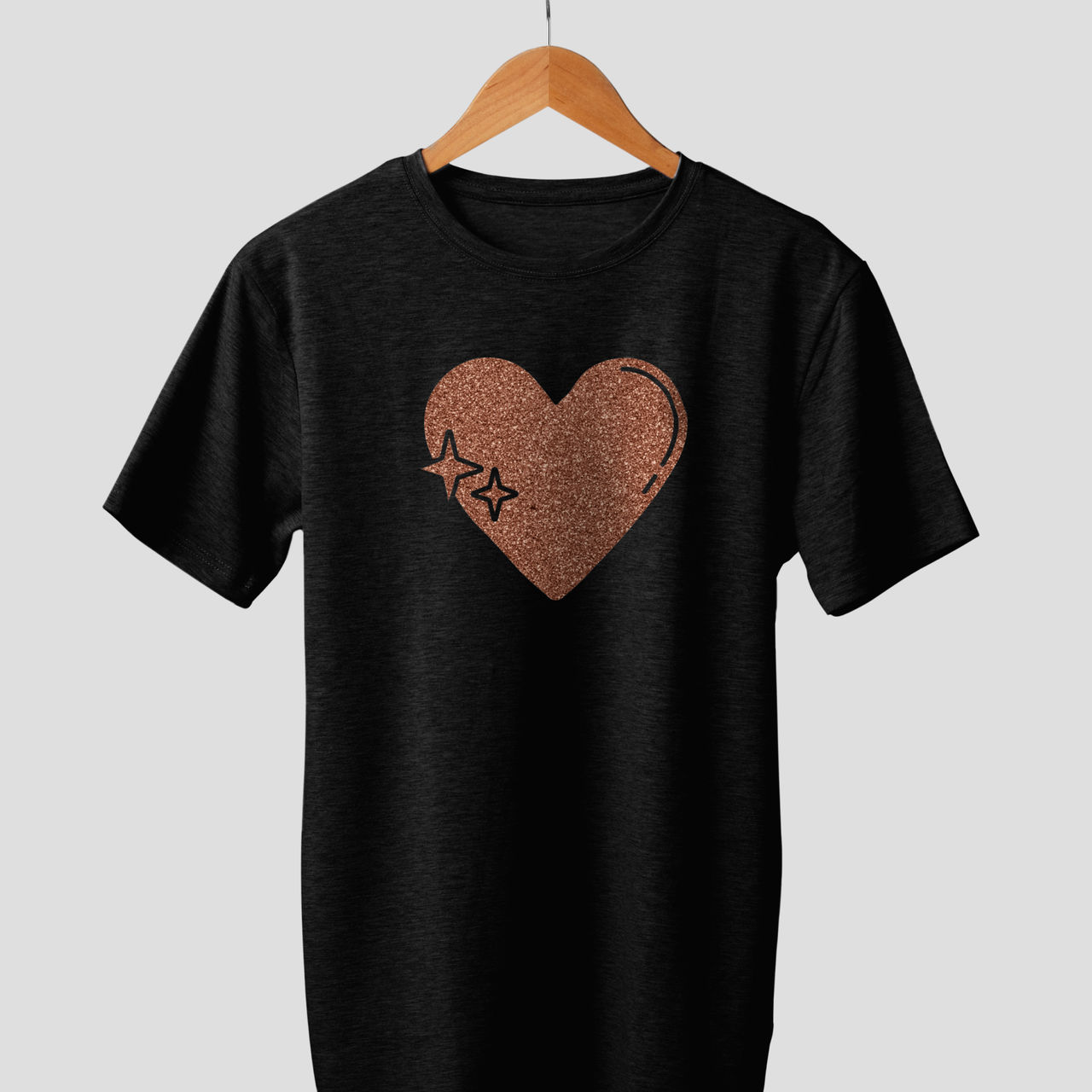 Schwarzes T-Shirt mit roségoldenem Herz- und Sterndesign, an einem Holzbügel.