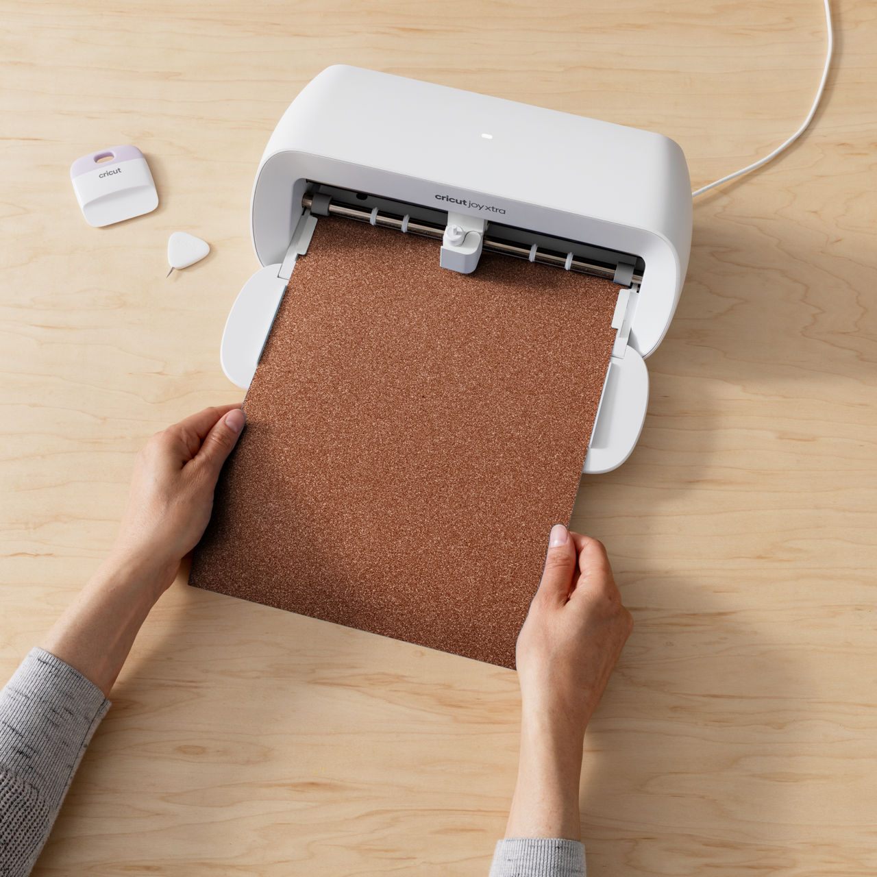 Eine Person, die ein braunes Blatt in eine weiße Cricut-Maschine einlegt.