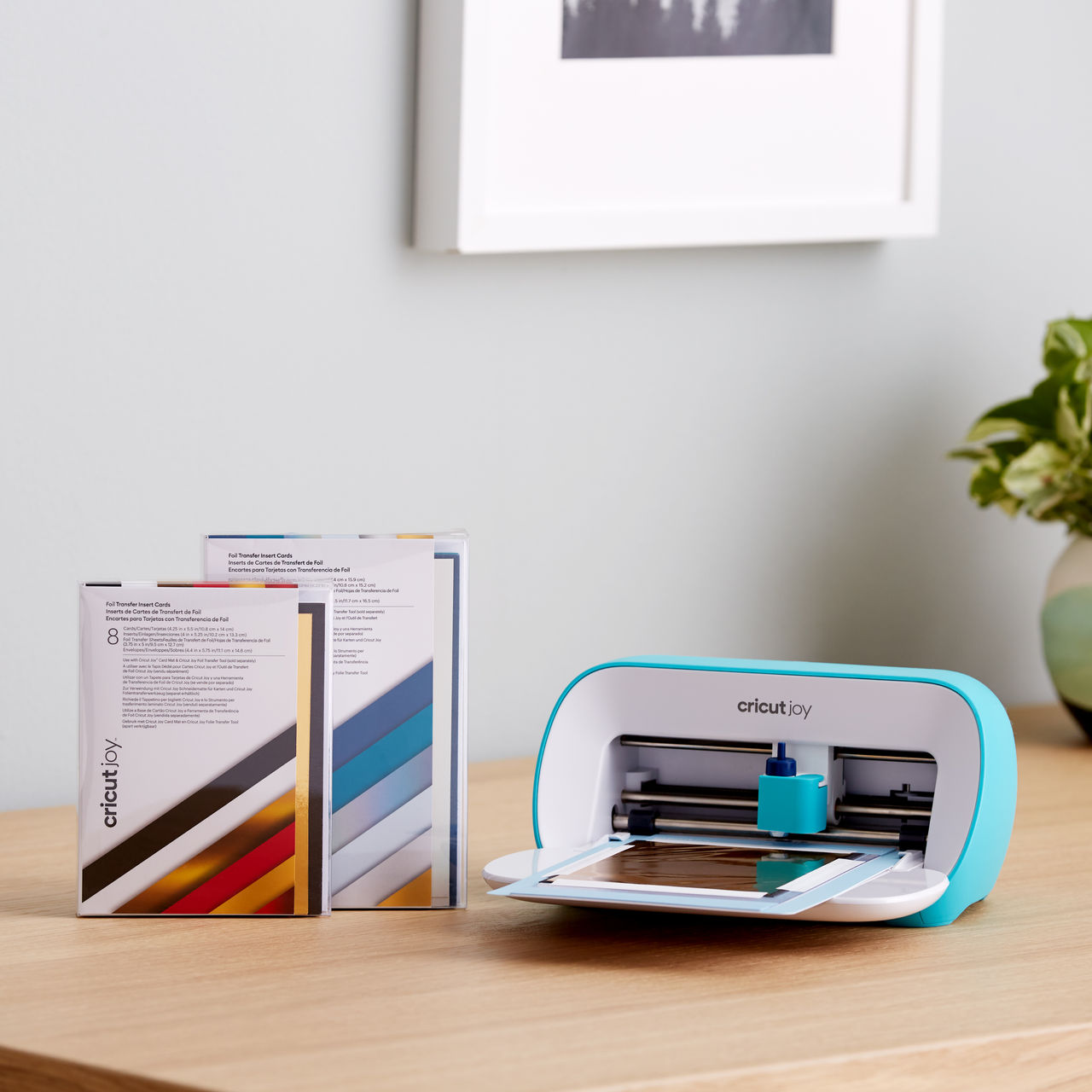 Cricut Joy und Cricut Joy Folien-Transfer-Einsatzkarten auf einem Holztisch in der Nähe einer Wand und eines Fensters.