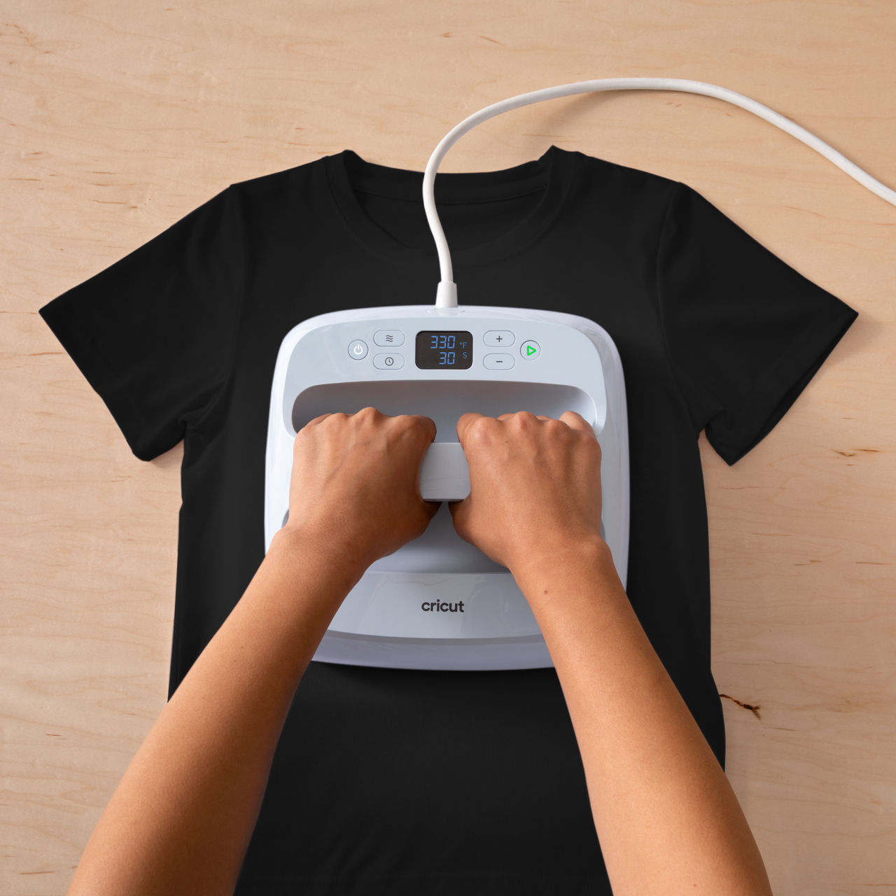Hände bügeln schwarzes T-Shirt mit weißem Cricut-Bügeleisen auf Holzoberfläche.