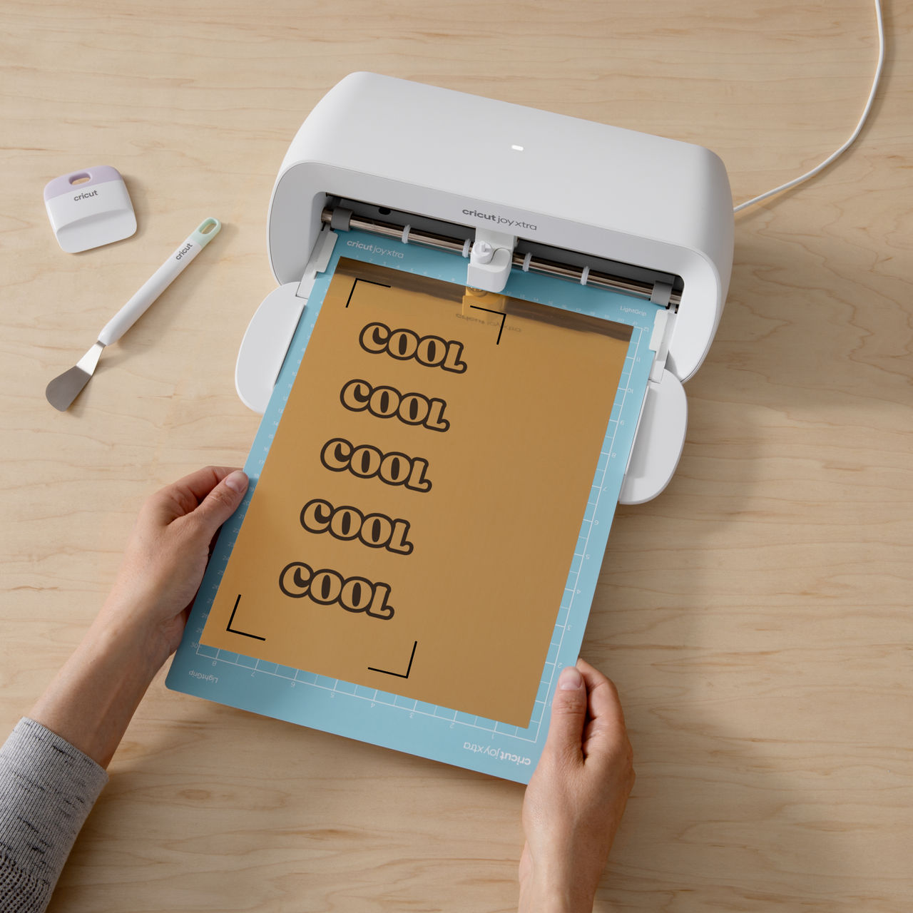 Eine Cricut Joy Xtra Maschine, die ein goldenes Blatt mit dem Wort 'COOL' hält.