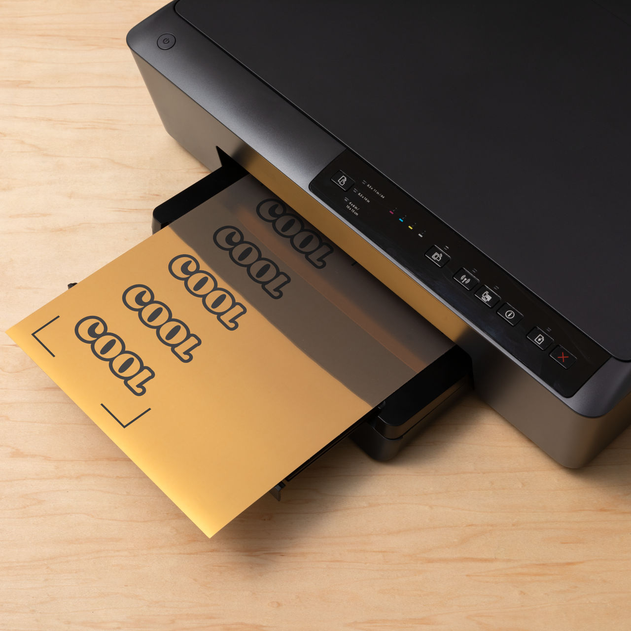 Ein schwarzer Drucker, der ein goldenes Blatt mit dem Wort 'COOL' auf einem Holztisch ausgibt.