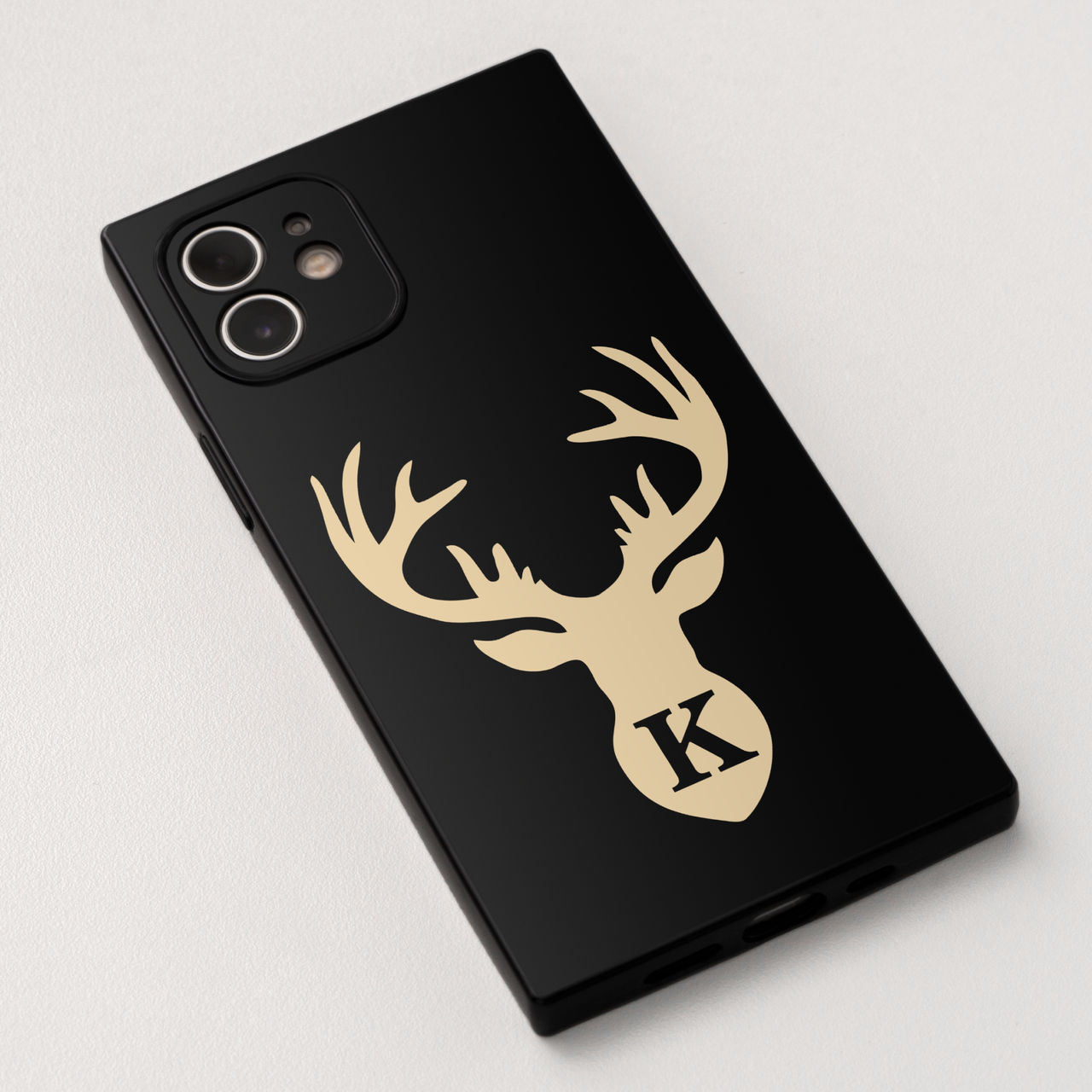 Eine schwarze Handyhülle mit einem goldenen Hirschkopf und dem Buchstaben 'K' auf weißem Hintergrund.