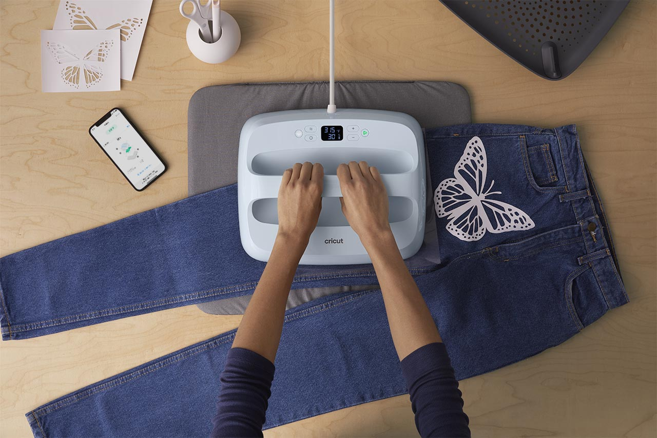 Hände benutzen Cricut-Maschine auf Jeans mit Schmetterlingsdesign. Andere Ausschnitte sichtbar.