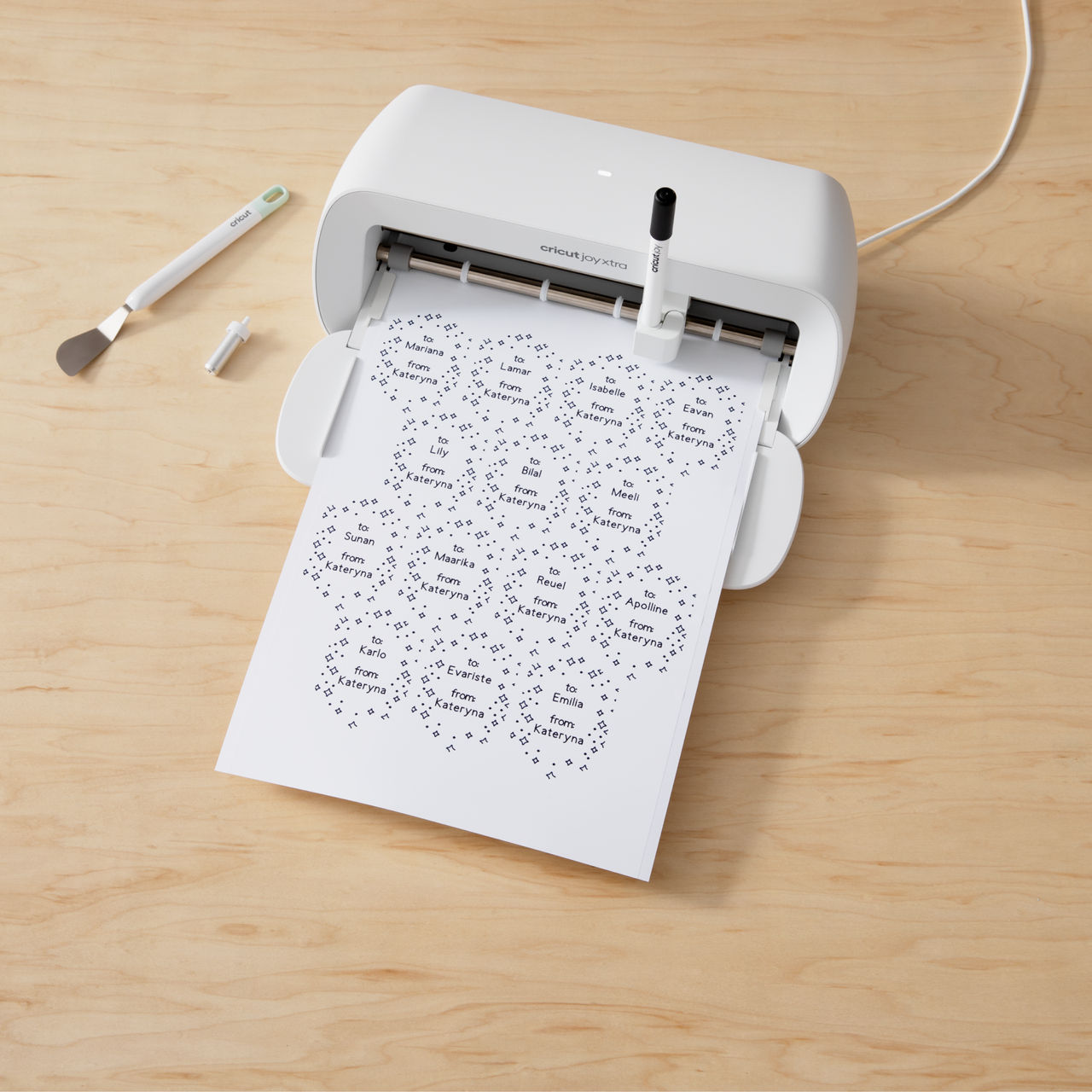 Weiße Cricut Joy Xtra Maschine, die auf ein weißes Blatt Papier druckt. Es gibt Etiketten und einen Spatel.
