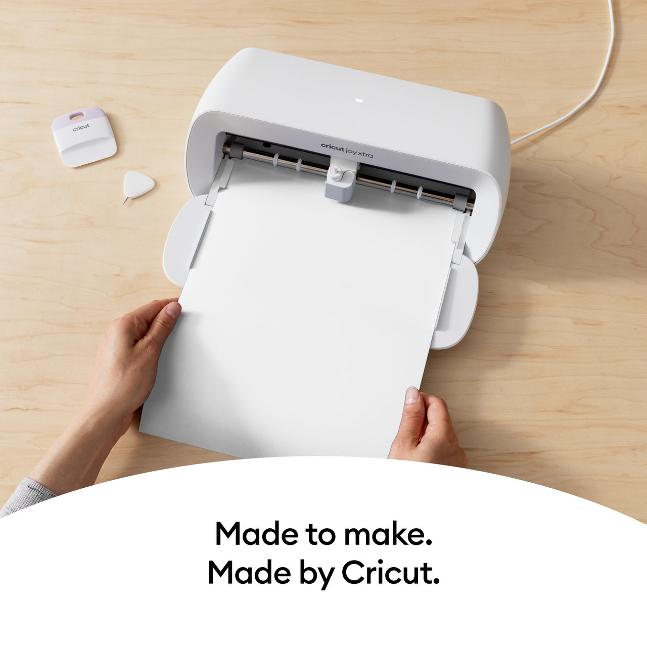 Cricut Joy Xtra Maschine schneidet weißes Papier. Hände halten das Papier. Holztisch.