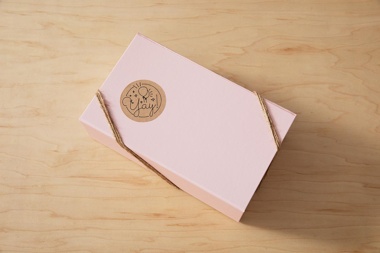 Rosa Geschenkbox mit Bindfaden verschnürt, mit einem runden Aufkleber mit 'yay'. Auf Holzoberfläche.