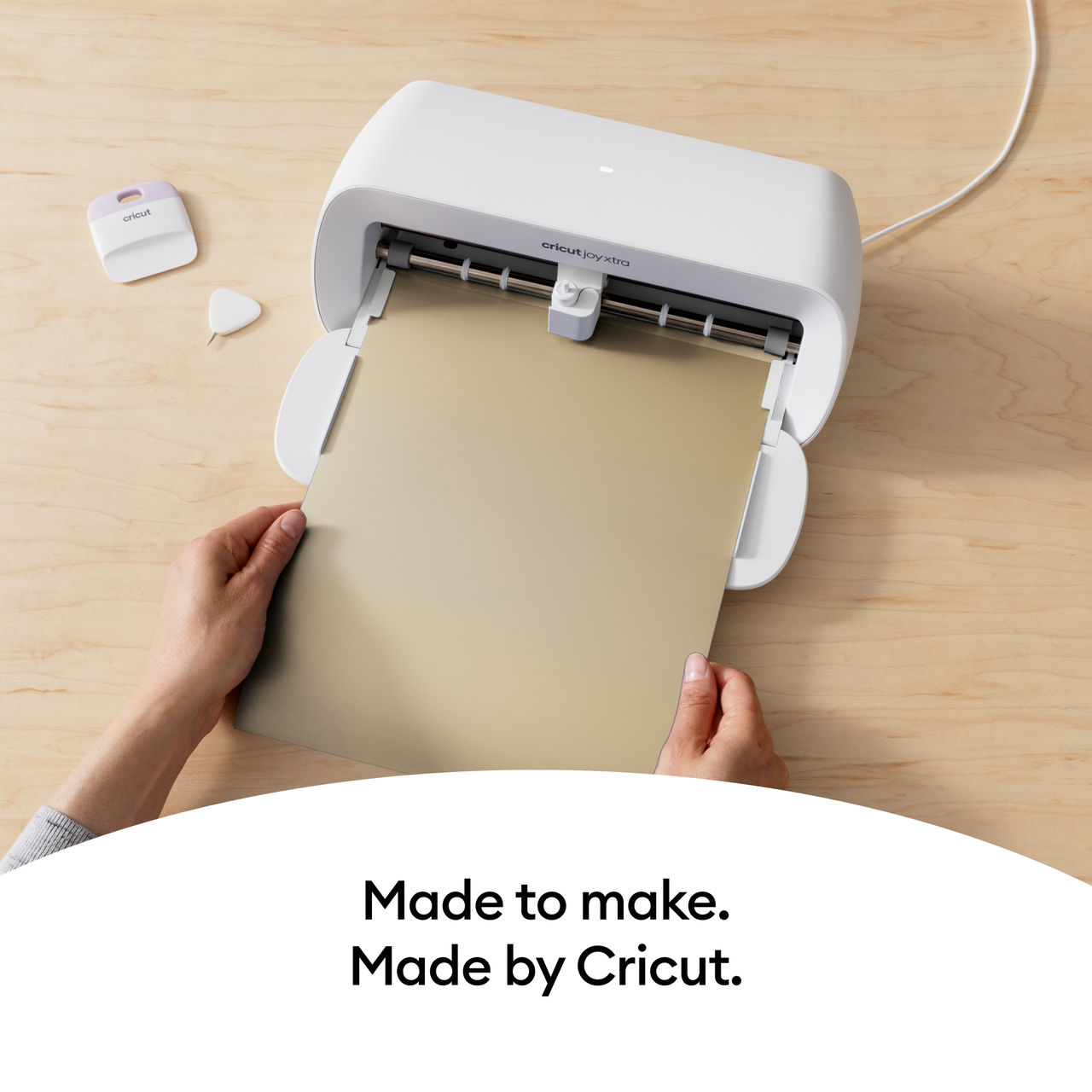 Cricut Joy Xtra Maschine und Werkzeuge. Hände, die goldenes Papier in die weiße Maschine einführen.