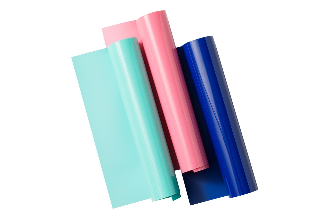Drei Rollen farbigen Vinyls: hellblau, rosa und dunkelblau, diagonal auf weißem Hintergrund angeordnet.