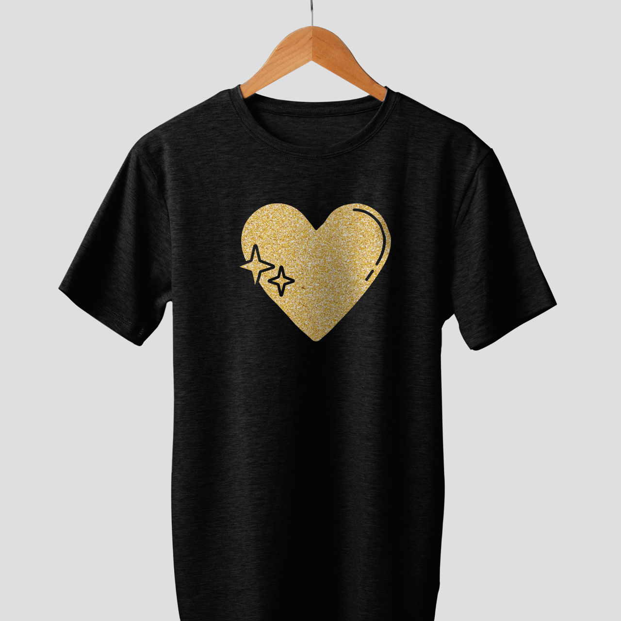 Ein schwarzes T-Shirt mit einem goldenen Herz und zwei Sternen-Design. Es hängt an einem Holzbügel.