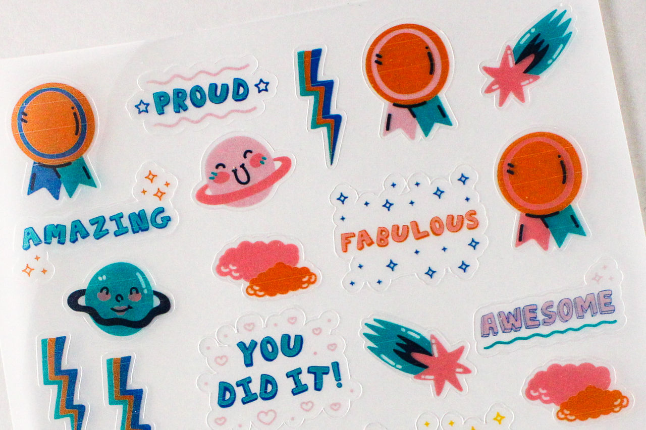 Aufkleberbogen mit bunten Designs: Planeten, Schleifen, Blitze und Sätze wie 'Amazing' und 'Fabulous'.