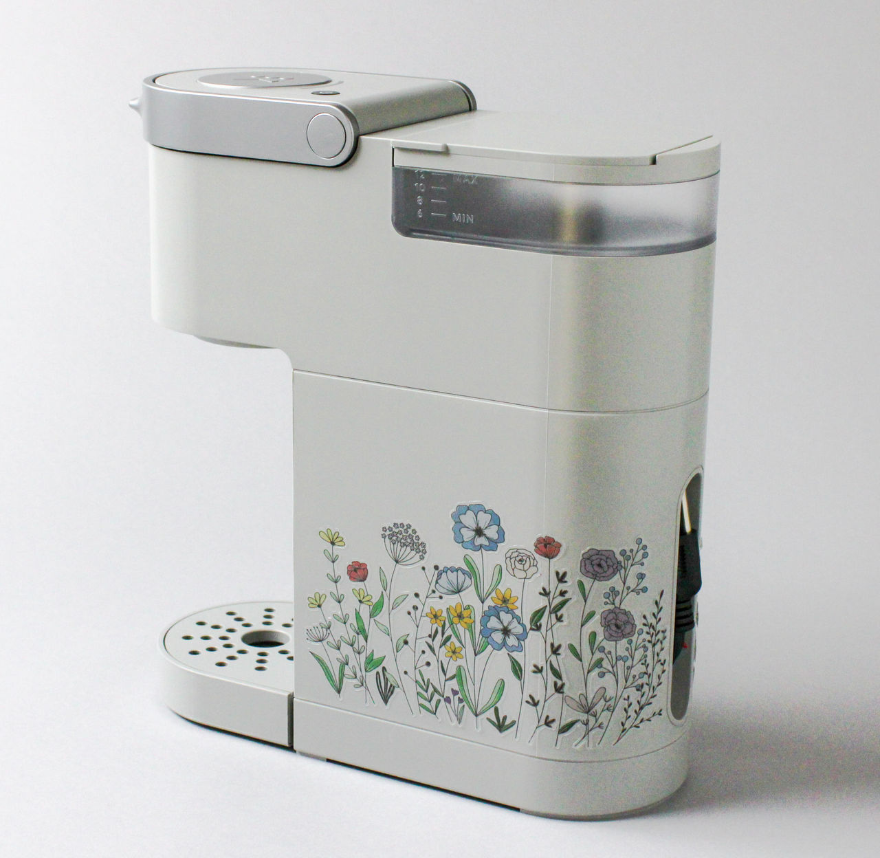 Weißer Kaffeemaschine mit floralem Design und einem Griff.