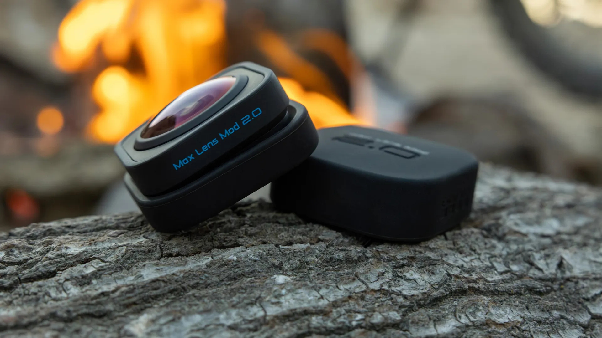 Czarny obiektyw na kłodzie. Czarna obudowa obok obiektywu. Płomienie w tle.