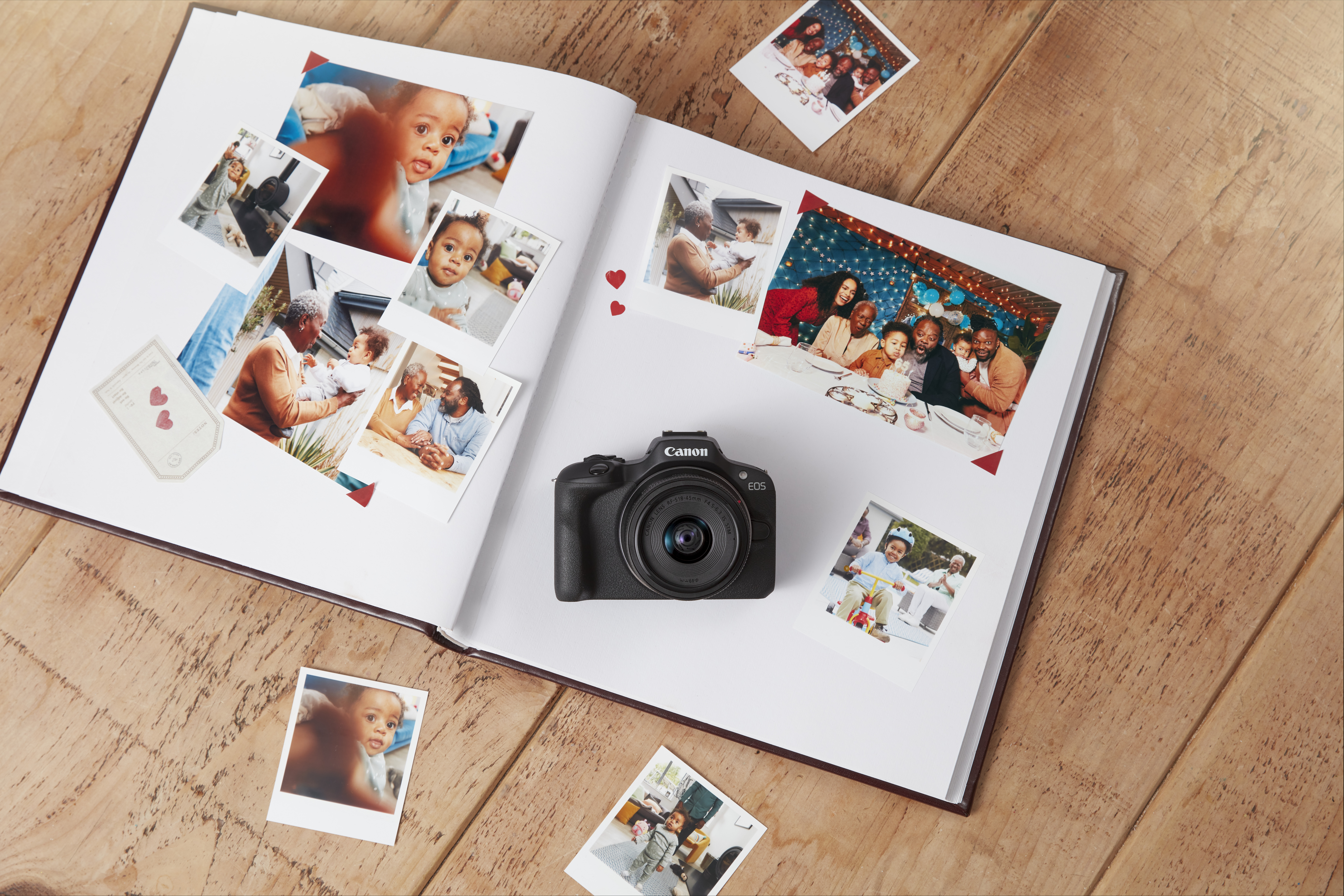 An open photo album with photos and a Canon camera on a wooden surface.