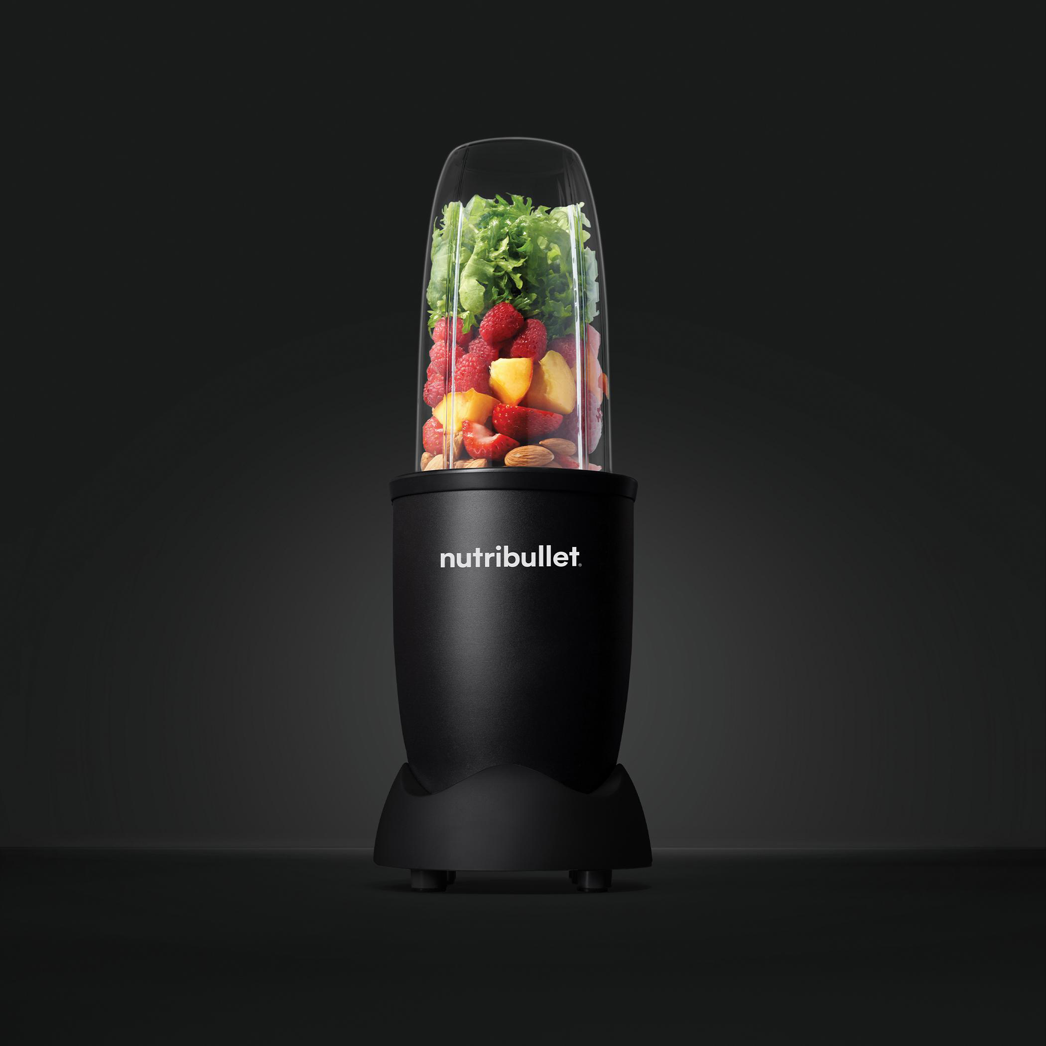 Schwarzer Mixer mit Früchten und Gemüse im Inneren. Es ist auf dunklem Hintergrund.