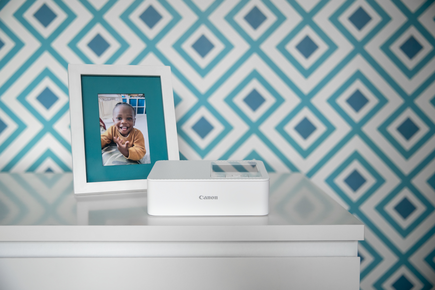Une photo encadrée d'un enfant, avec une imprimante photo Canon blanche sur une table blanche.
