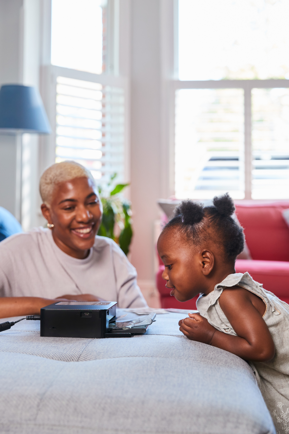 Une femme et un enfant en bas âge regardant une imprimante noire sur une table, à l'intérieur.