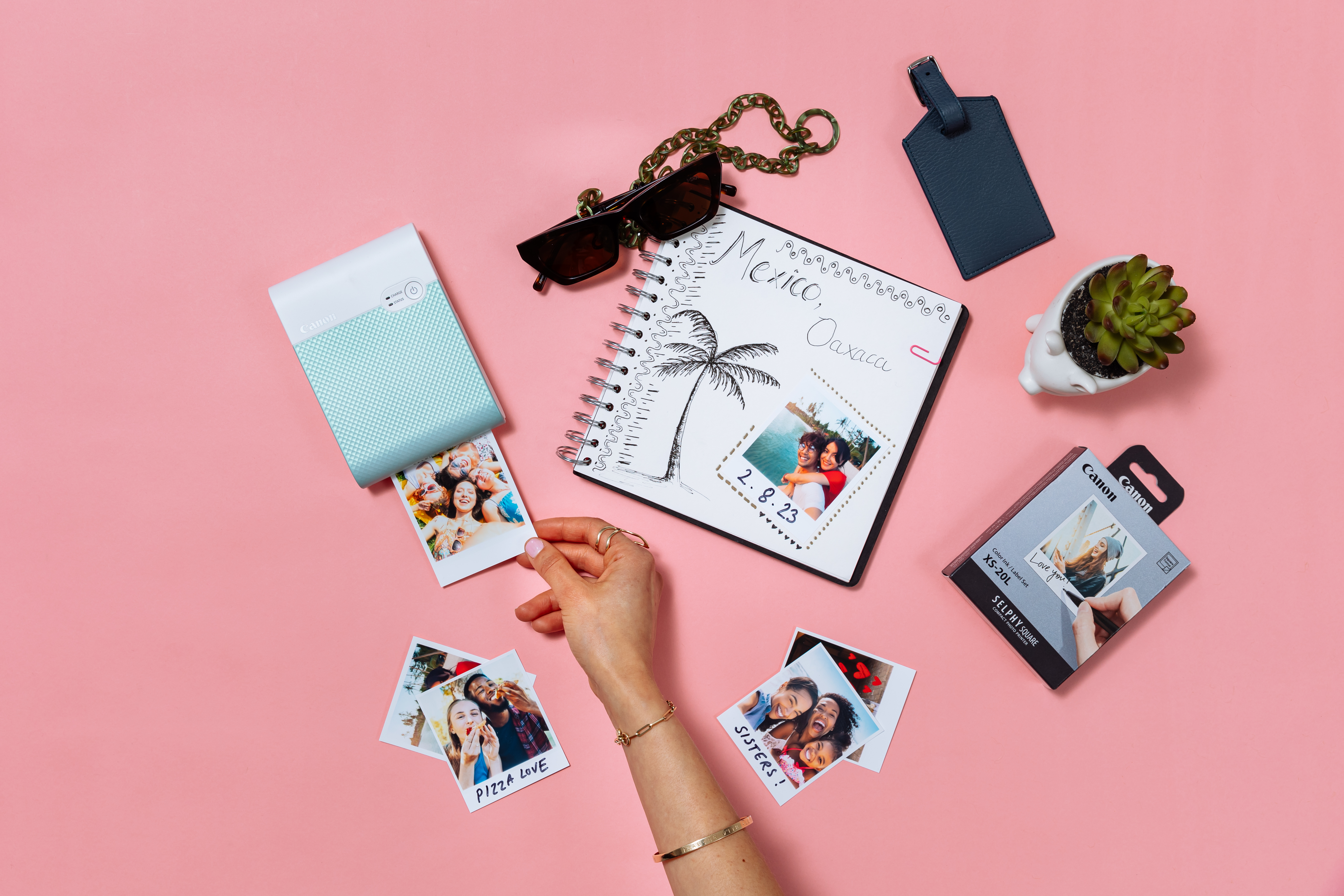 Imprimante photo, photos, accessoires et une main tenant une photo sur une surface rose.