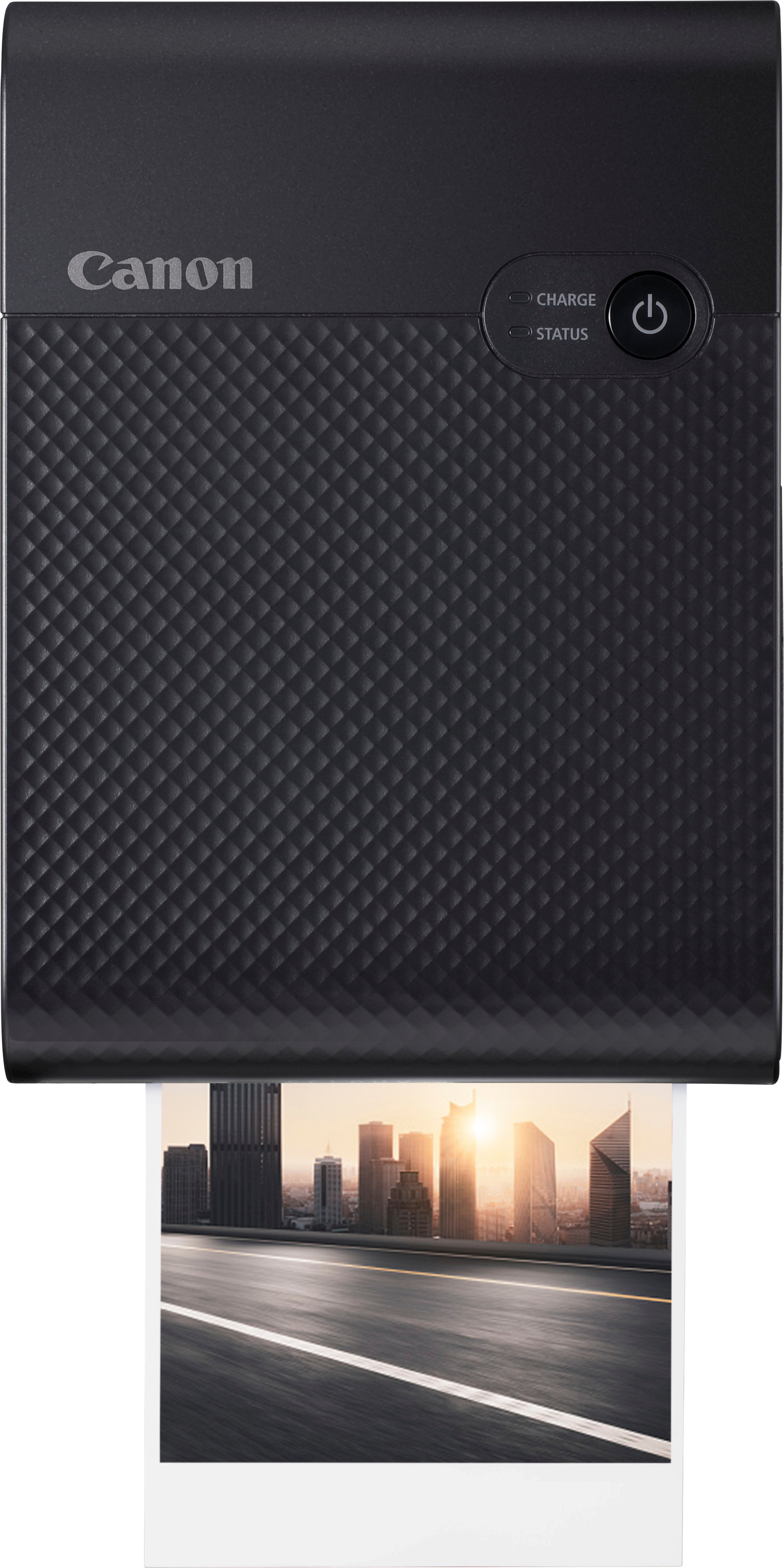 Une imprimante Canon noire imprime une photo d'un paysage urbain. L'imprimante est sur une surface blanche.