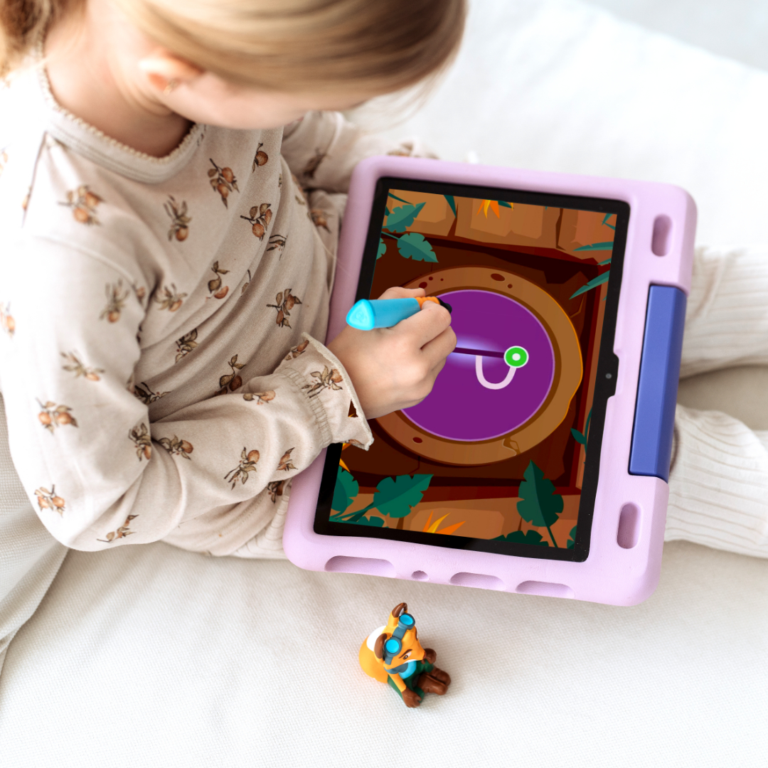 Ein Mädchen sitzt und benutzt ein Tablet mit rosa Hülle. Ein Spielzeugfuchs und ein Stift liegen auf dem Tisch.