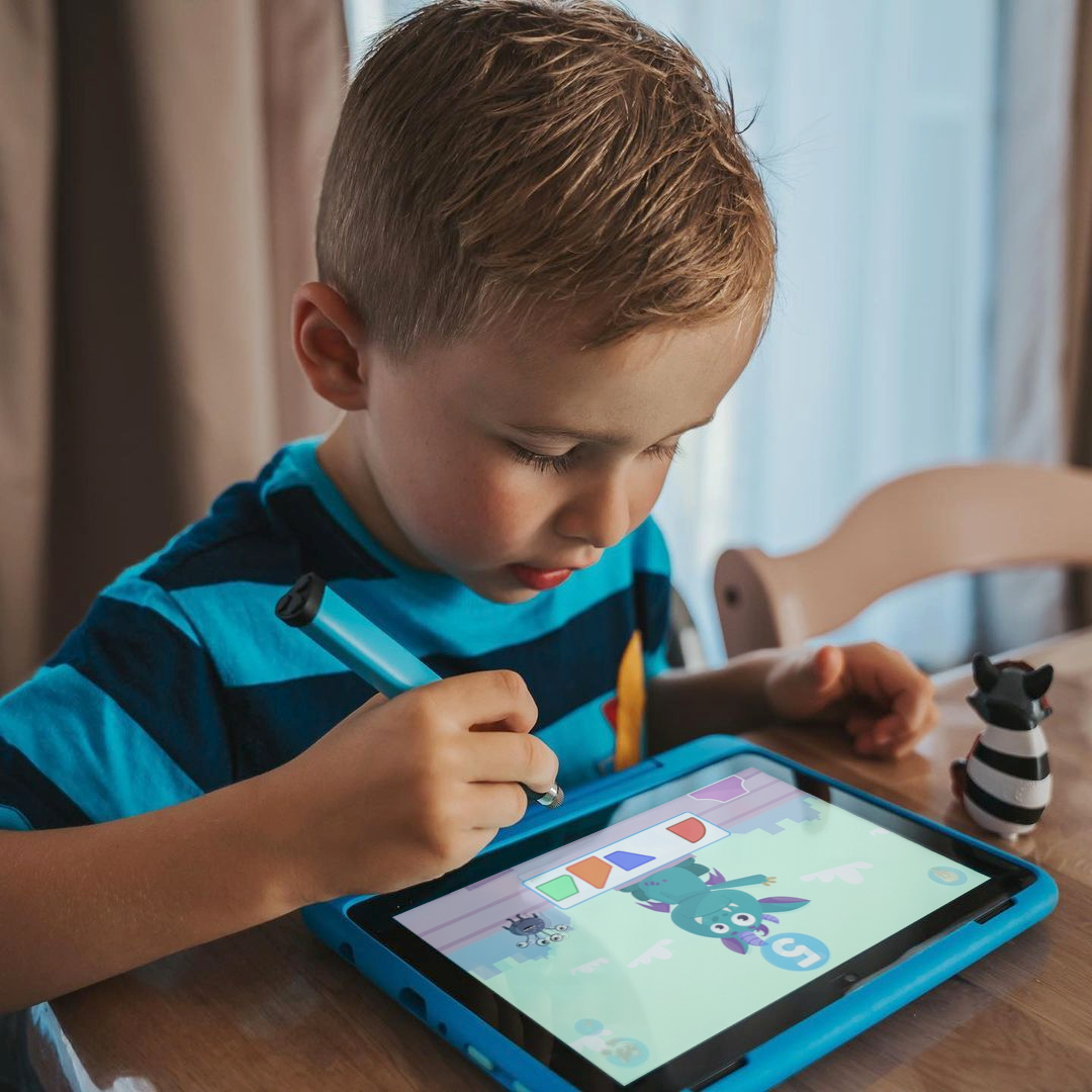 Junge benutzt Stift auf Tablet, Zebrafigur auf Tisch. Tablet zeigt Spiel.