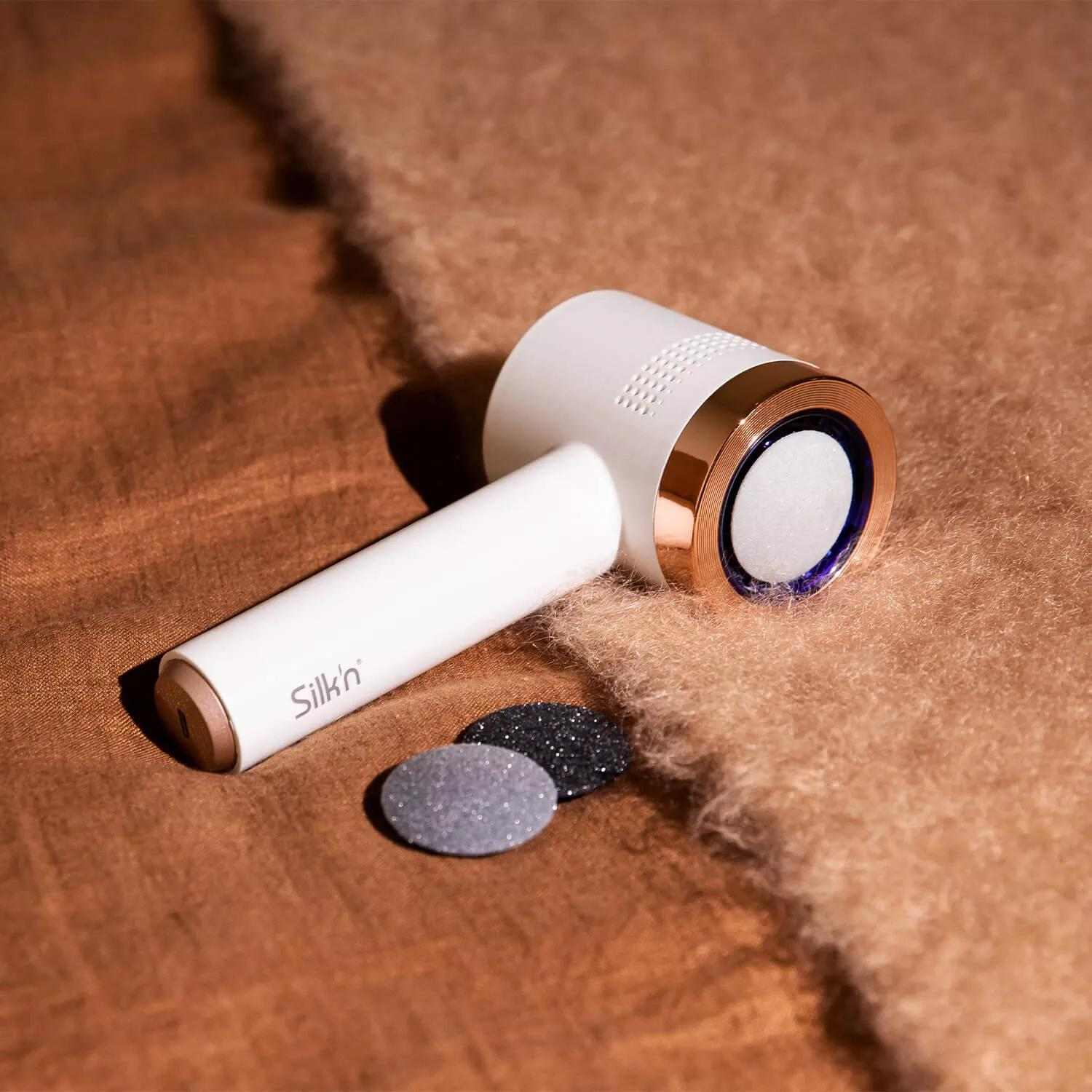 Biało-złote urządzenie z dwoma szarymi podkładkami. Służy do usuwania martwego naskórka.