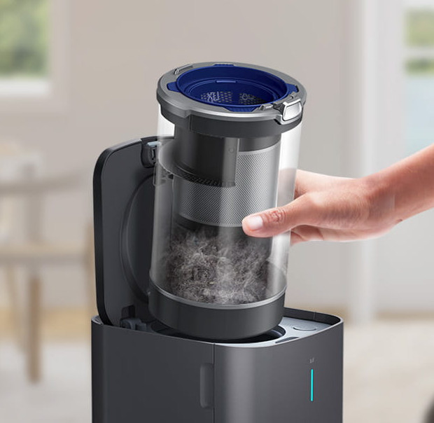 Ręka wyjmująca pojemnik na kurz z podstawy odkurzacza.