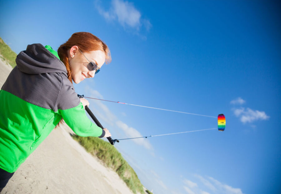 Nő sárkányt reptet a strandon, kék ég a háttérben. A sárkány többszínű.