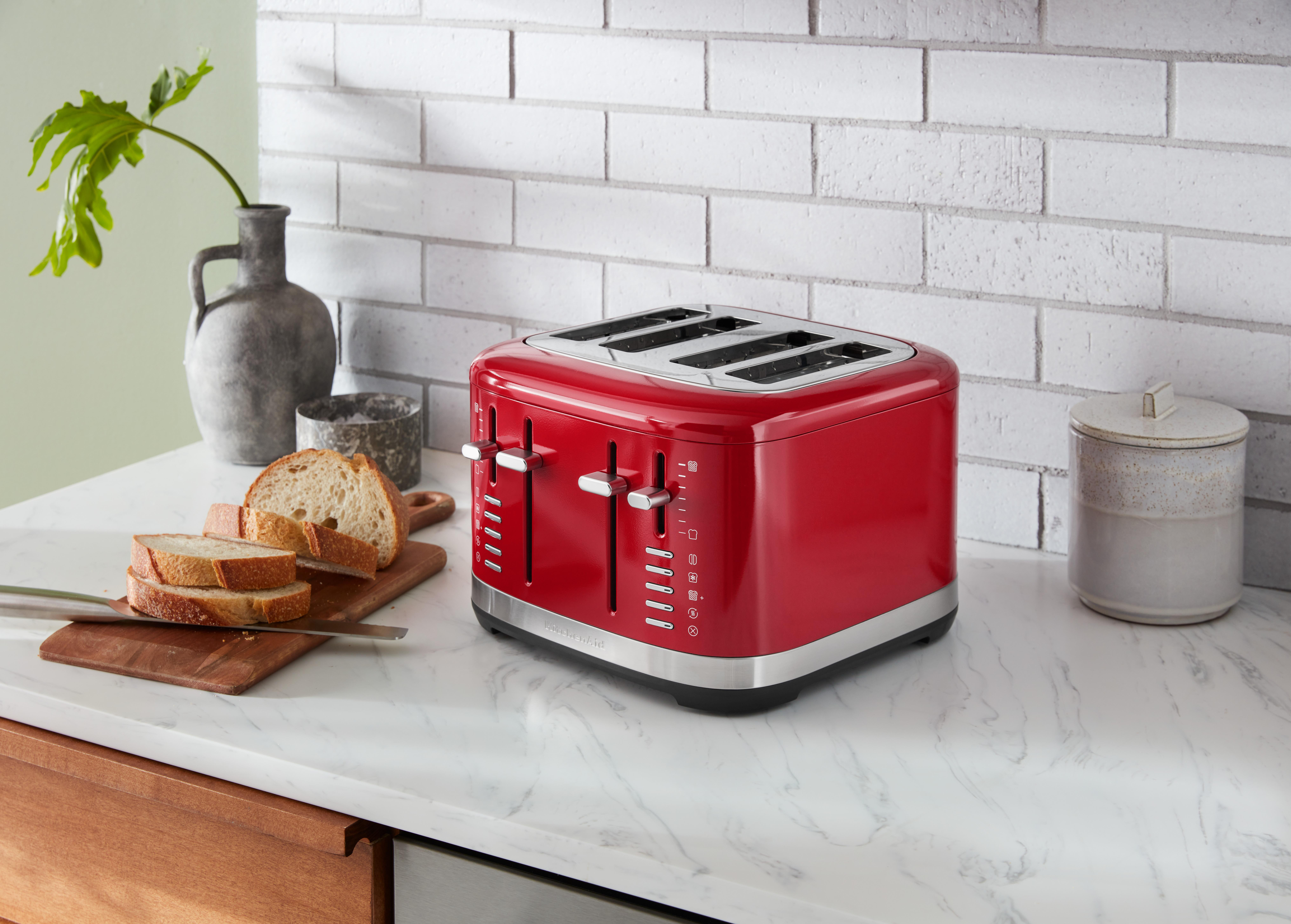 Ein roter 4-Schlitz-Toaster auf einer Marmor-Arbeitsplatte, mit Brot und einem Glas.