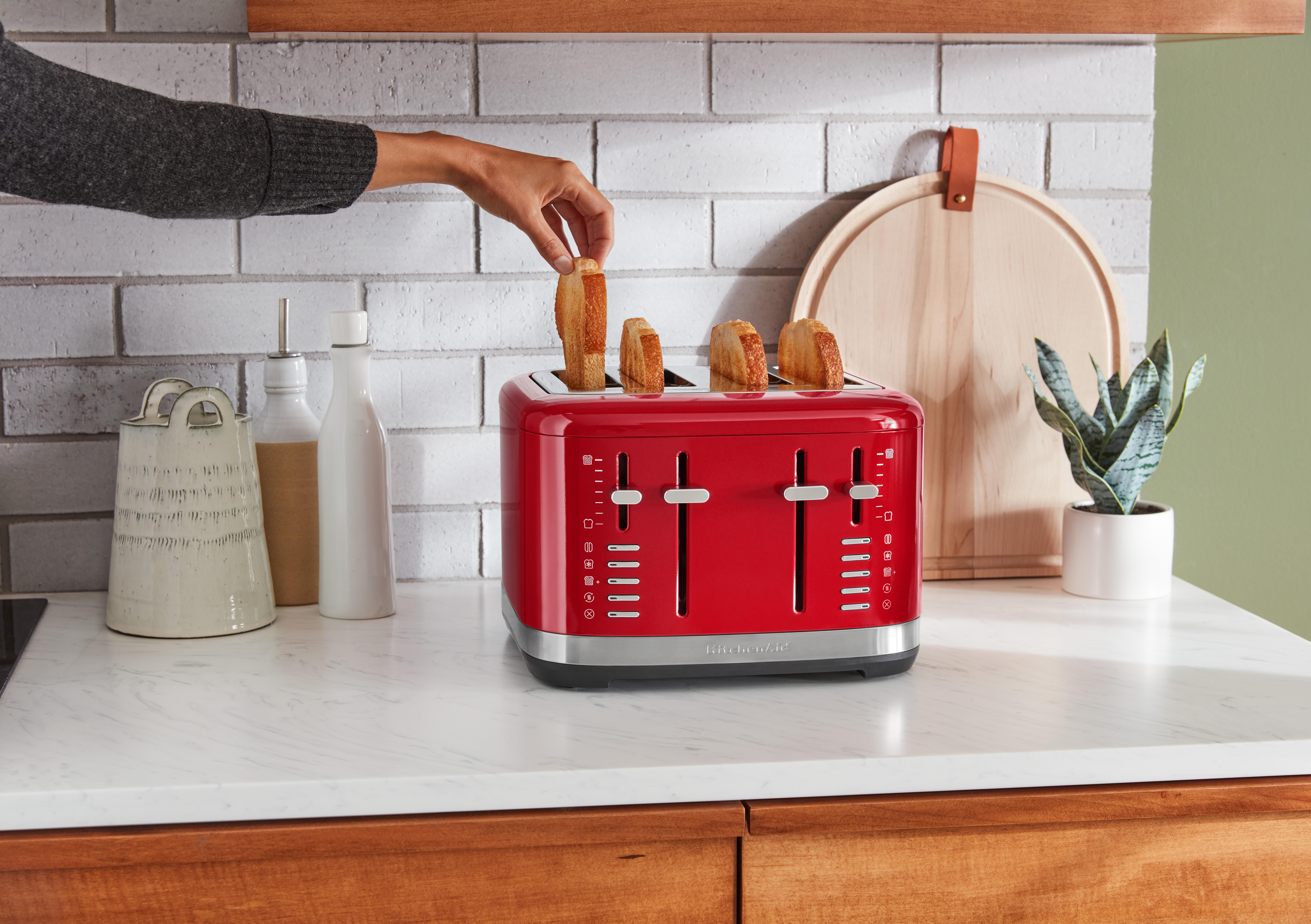 Ein roter KitchenAid-Toaster mit Toast, der auf einer weißen Arbeitsplatte hineingelegt wird.