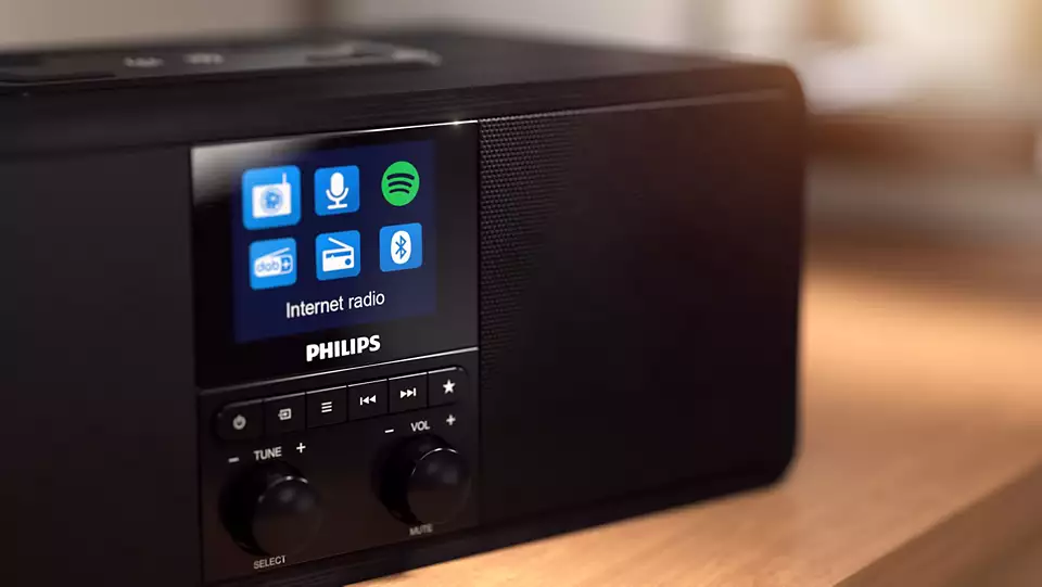 Radio Internet Philips noire avec écran affichant des icônes et des commandes. Table en bois au premier plan.