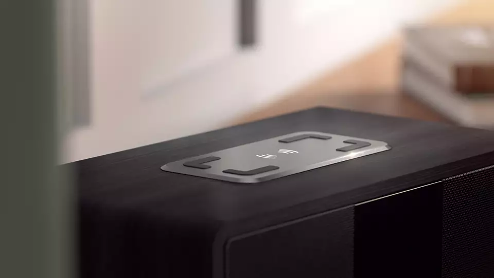 Un haut-parleur noir avec un dessus argenté qui porte le symbole de la recharge sans fil.
