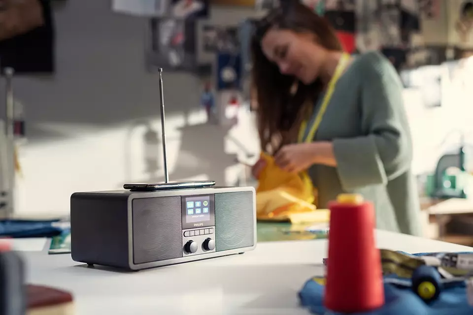 Radio sur une table. Une femme travaille en arrière-plan. La radio a un écran et des boutons.