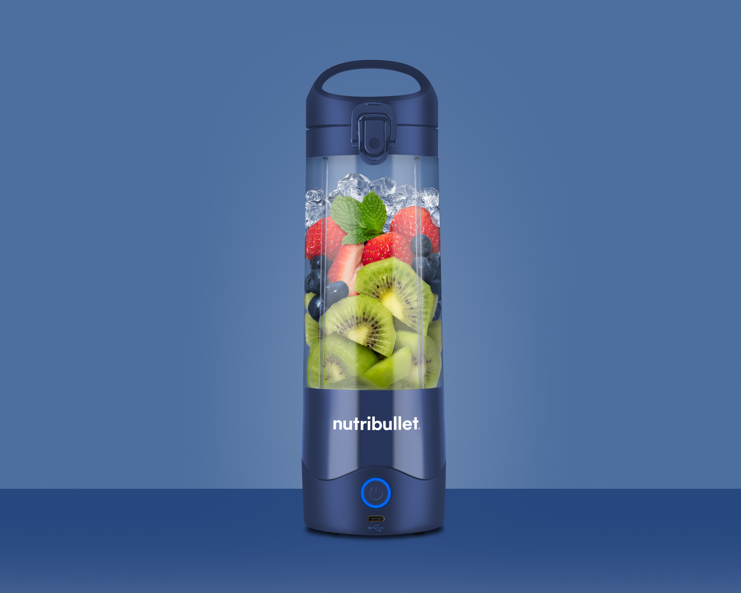 Una licuadora Nutribullet azul llena de hielo, fresas, kiwi y arándanos.