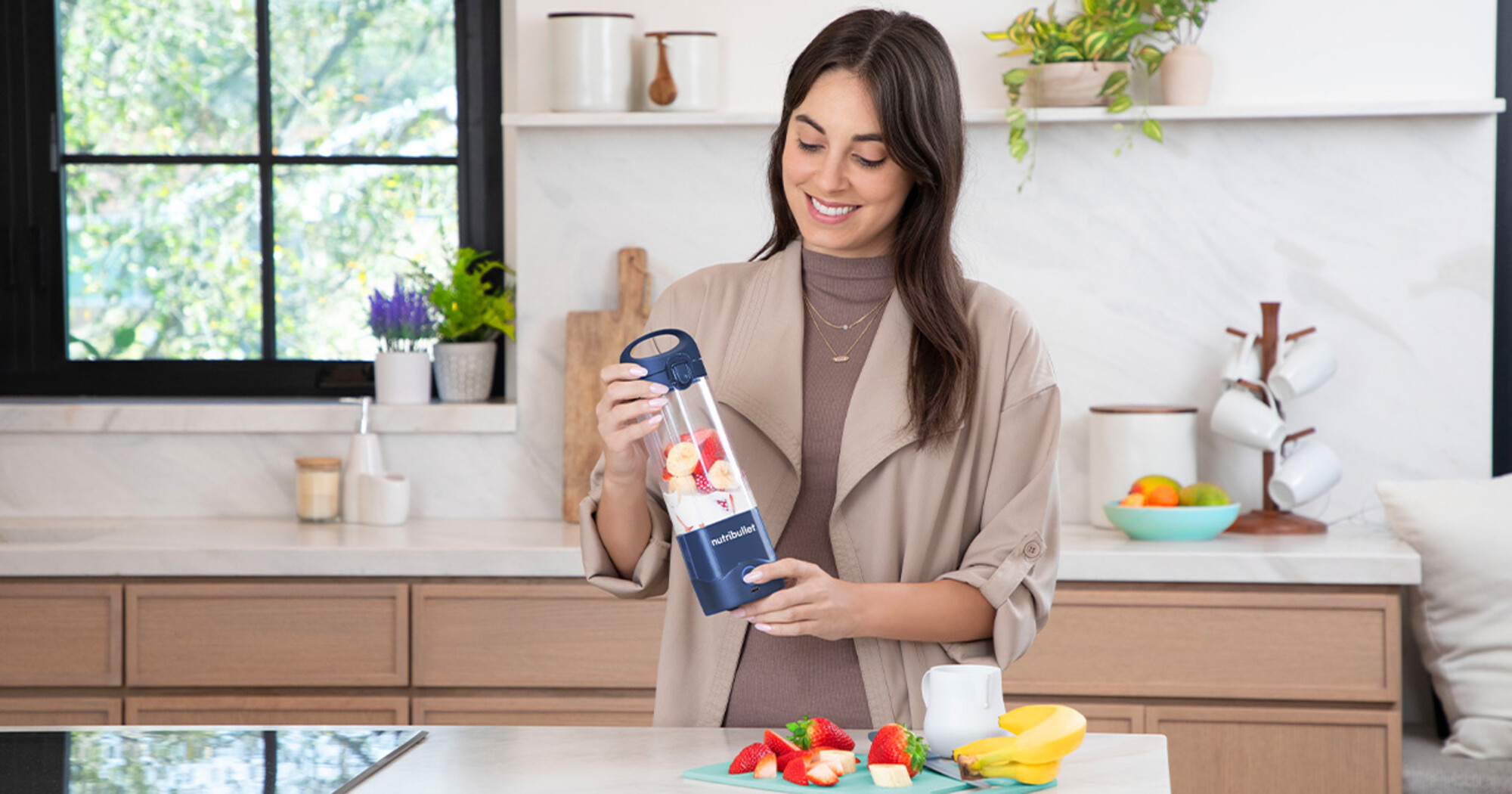 Mujer en la cocina sosteniendo una licuadora con fruta dentro.