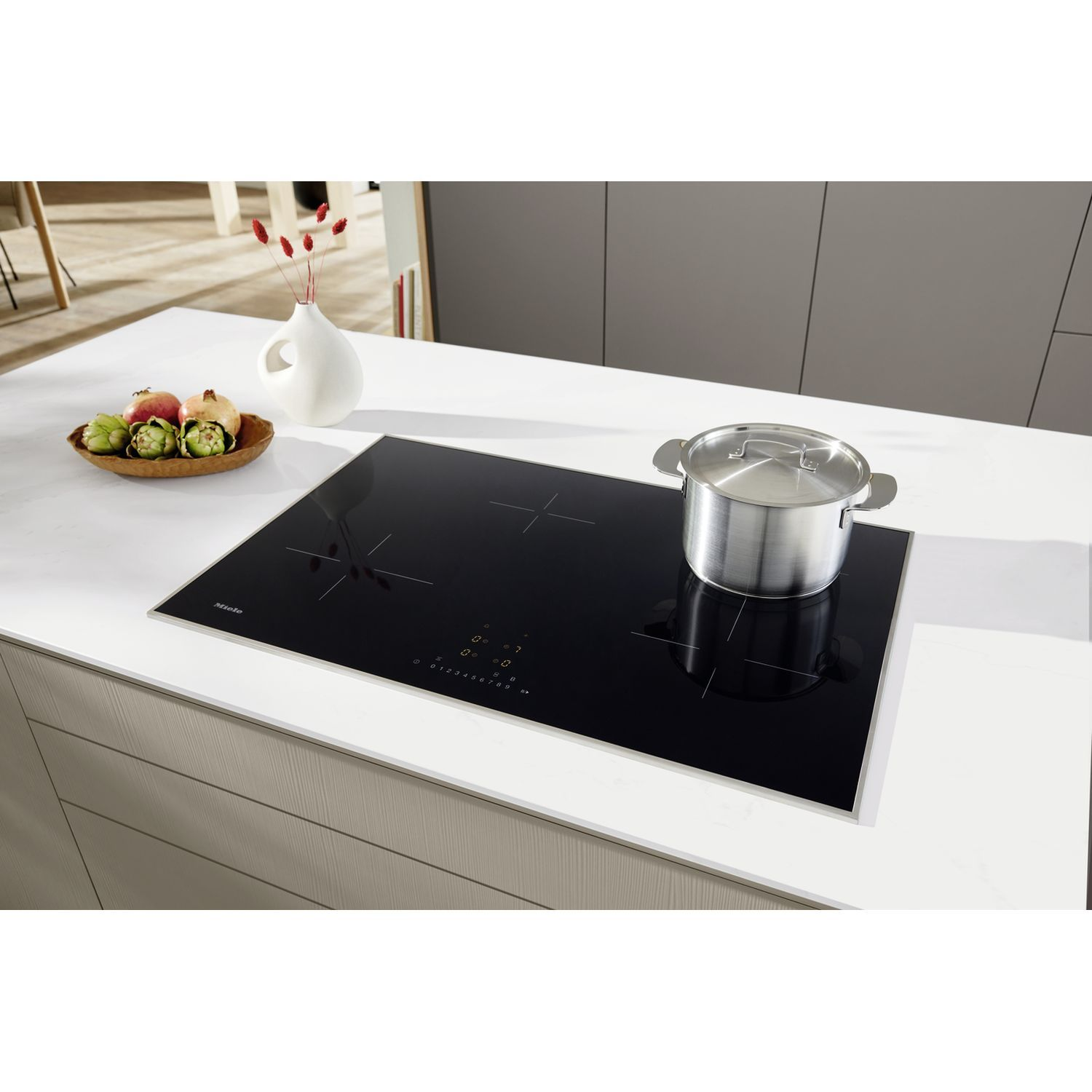 Table de cuisson noire avec une casserole dessus. Un comptoir blanc et un meuble en bois sont dans la scène.
