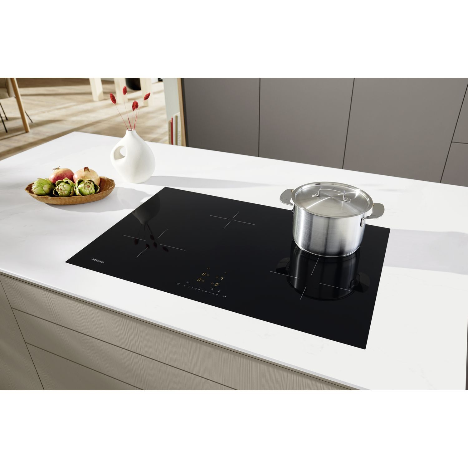 A silver pot on a black induction hob next to a fruit bowl.