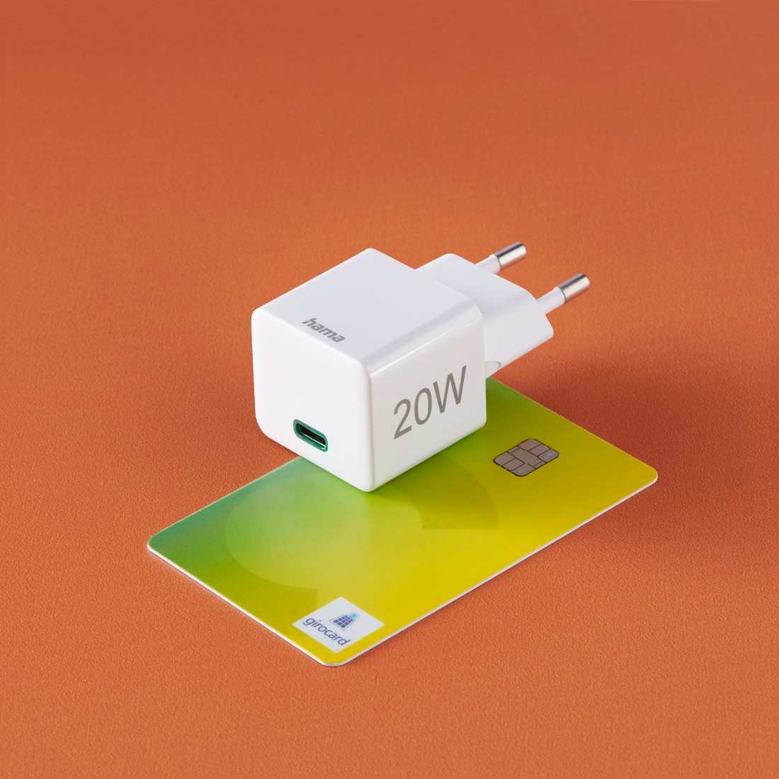 Fehér 20W-os töltő USB-C porttal, zöld kártyán és narancssárga háttérrel.