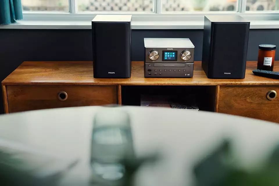 Mini sistema hi-fi con altoparlanti su mobile in legno, finestra sullo sfondo.