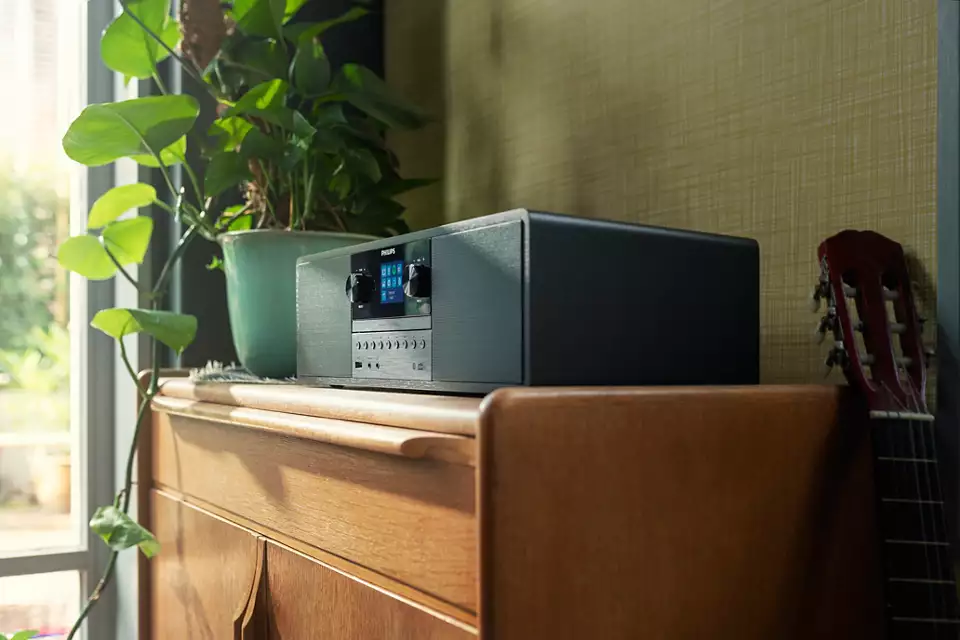 Un impianto stereo è su un mobile di legno, con una pianta in vaso a sinistra e una chitarra a destra.
